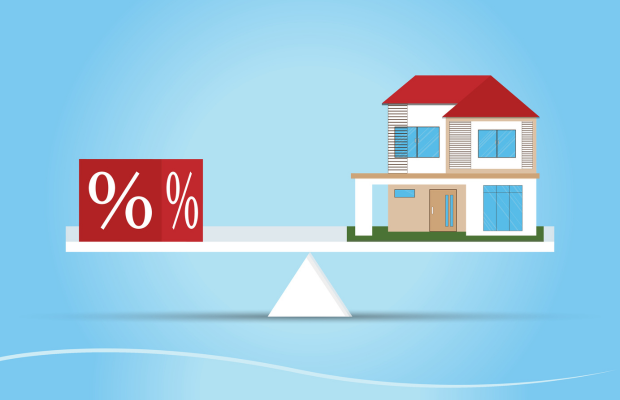 House balanced on a seesaw with a red block displaying two percent symbols on the left, suggesting a mortgage rate or home discount offer.