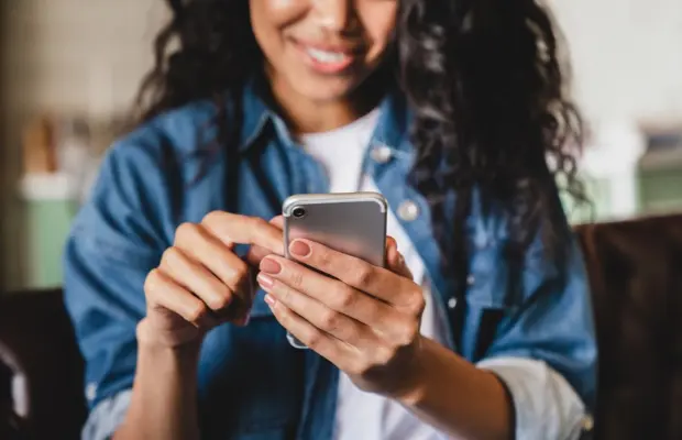 Person holding a smartphone and tapping the screen with one finger, smiling slightly.